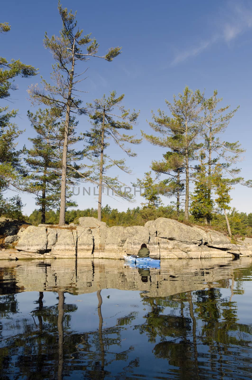 Kayaker checks the Canadian Shield rock formation on a calm tranquil northern lake in September