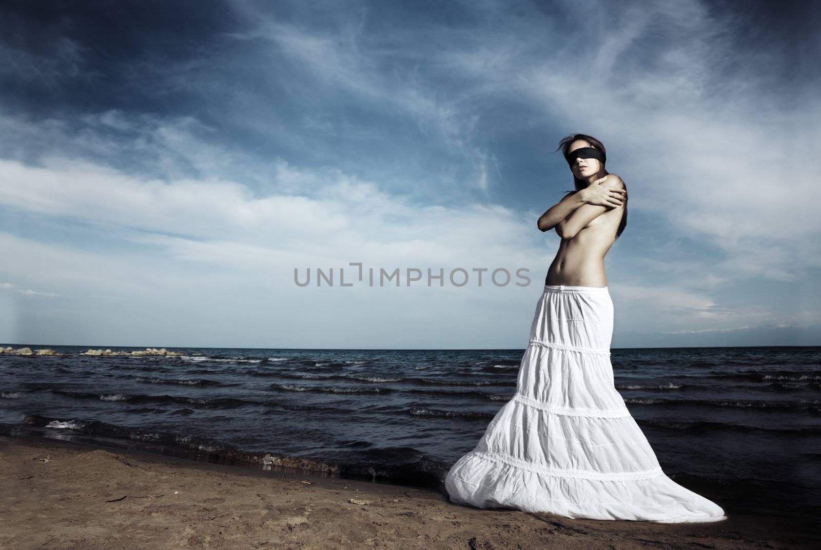 Lonely topless woman with blindfold standing at the beach