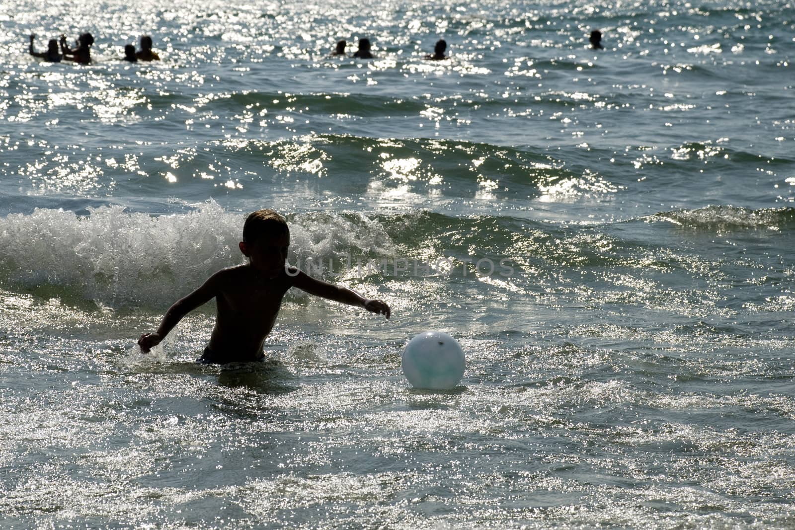 Boy reaching for the beachball through the waves.