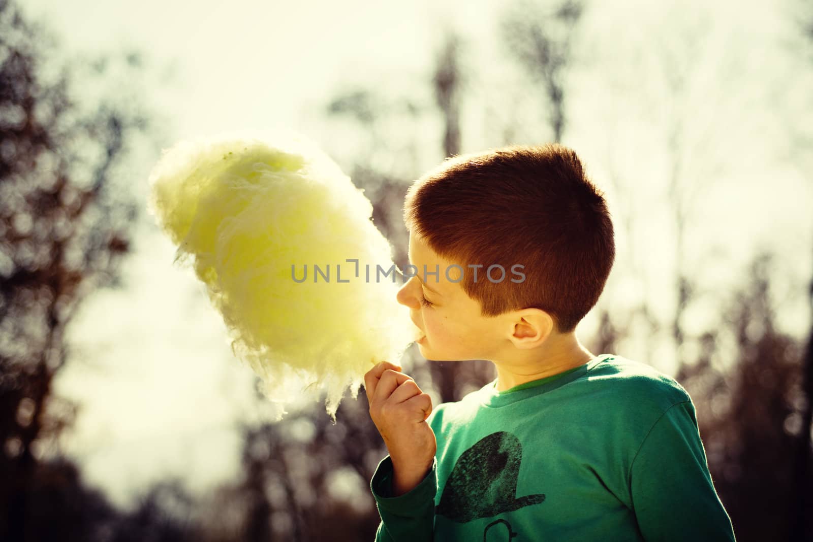 Young boy eating sugarwool in a park backlit