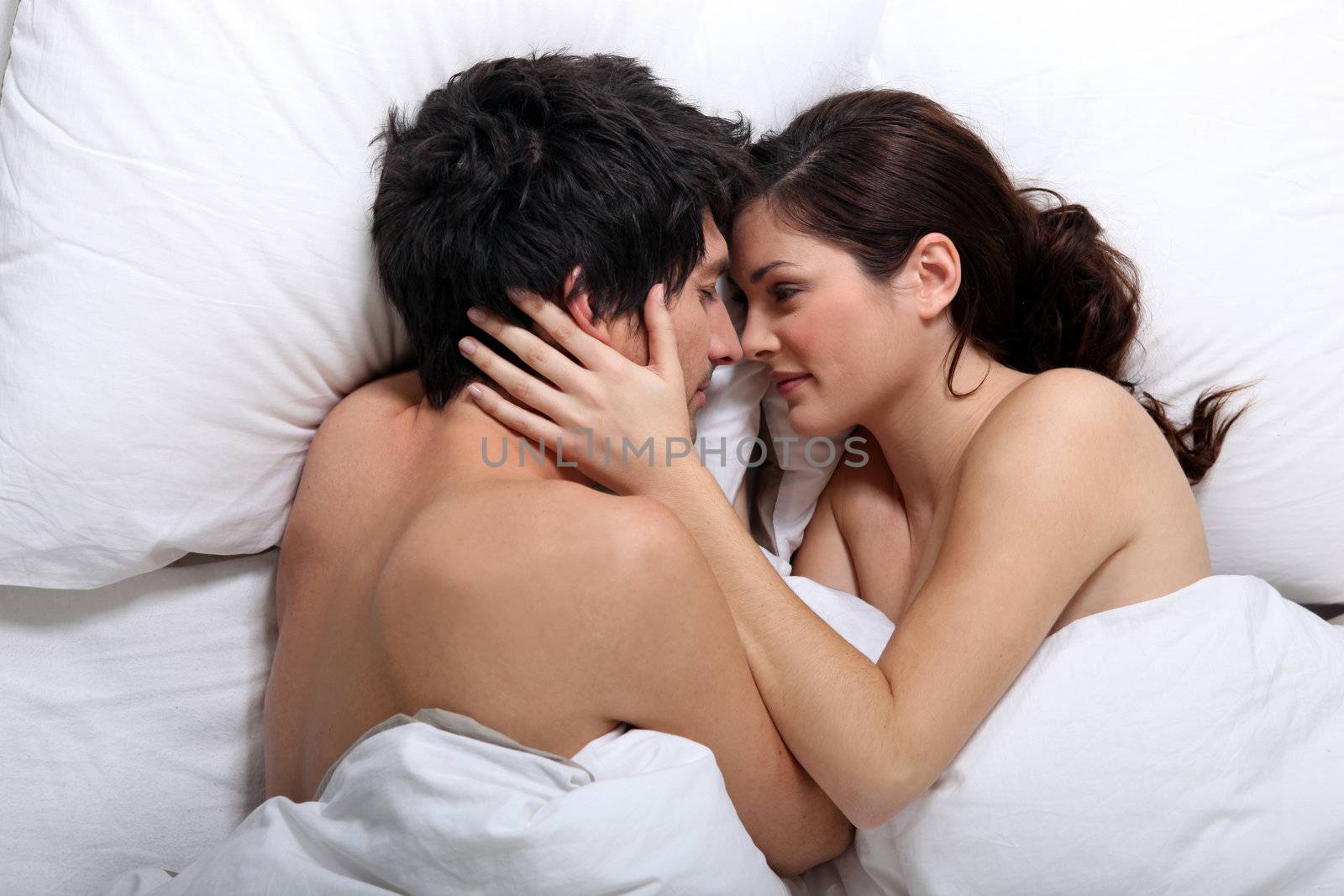 Affectionate couple kissing in bed by phovoir