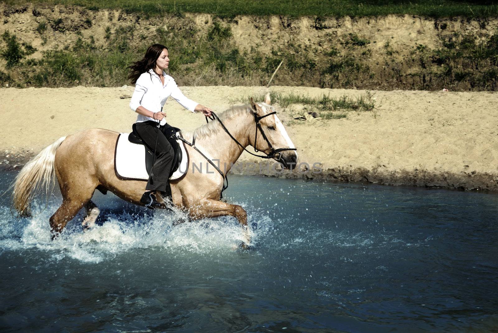 Photo of the woman riding on the horse through the river