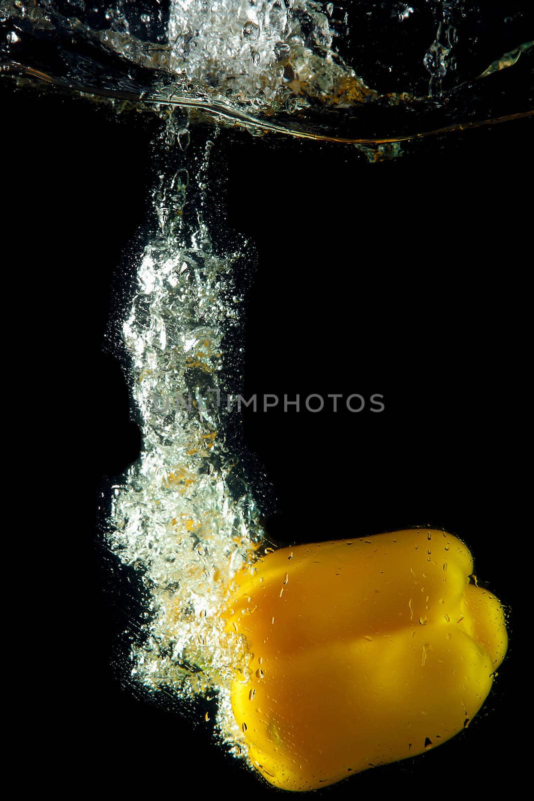 Colored yellow paprika in water splashes on black background