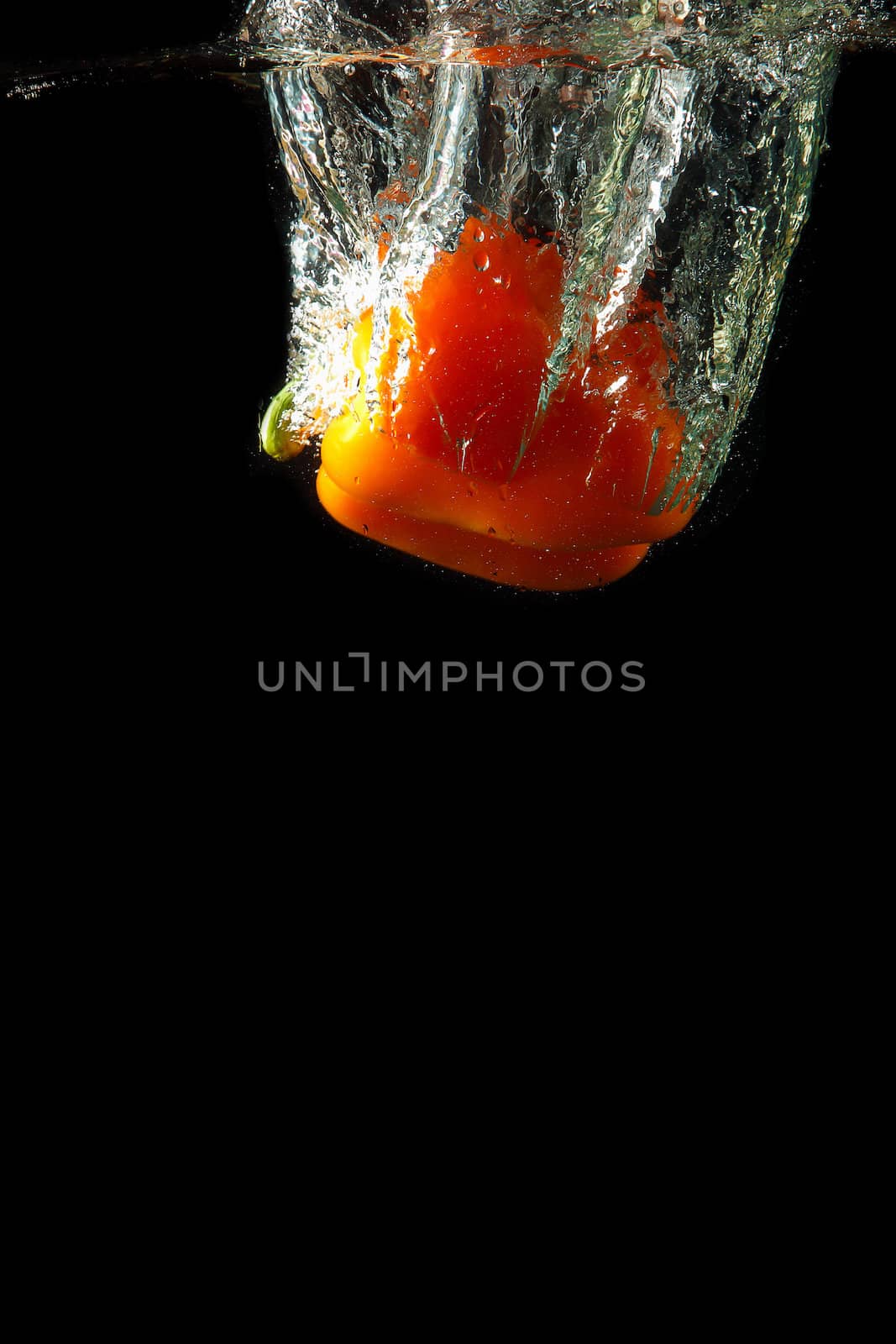 Colored orange paprika in water splashes on black background