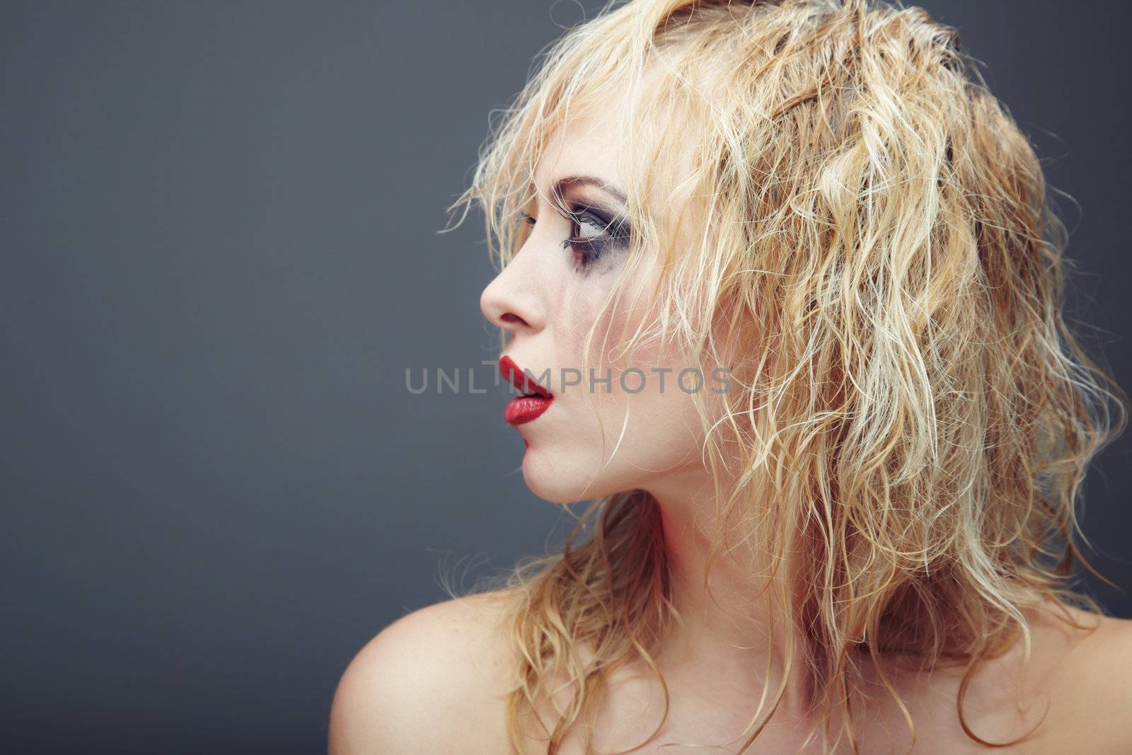 Beautiful blond lady with strange makeup. Side-view photo on a dark gray background. Artistic colors added