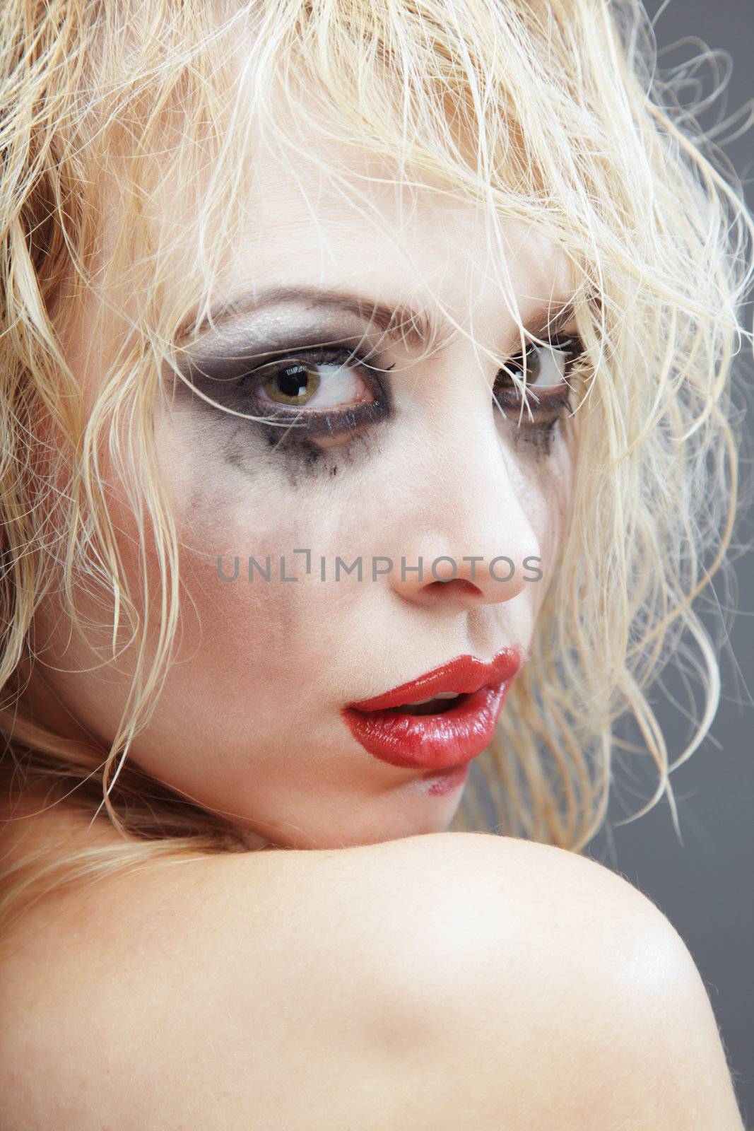 Turning back blond woman with bizarre makeup. Headshot photo in the studio