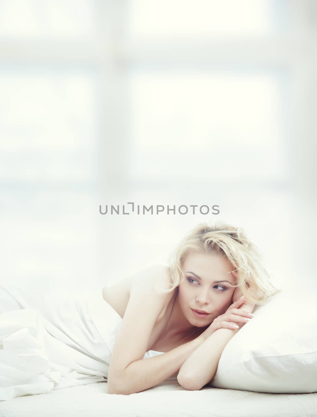 Blond lady laying in bedrrom at early morning. Window on the background