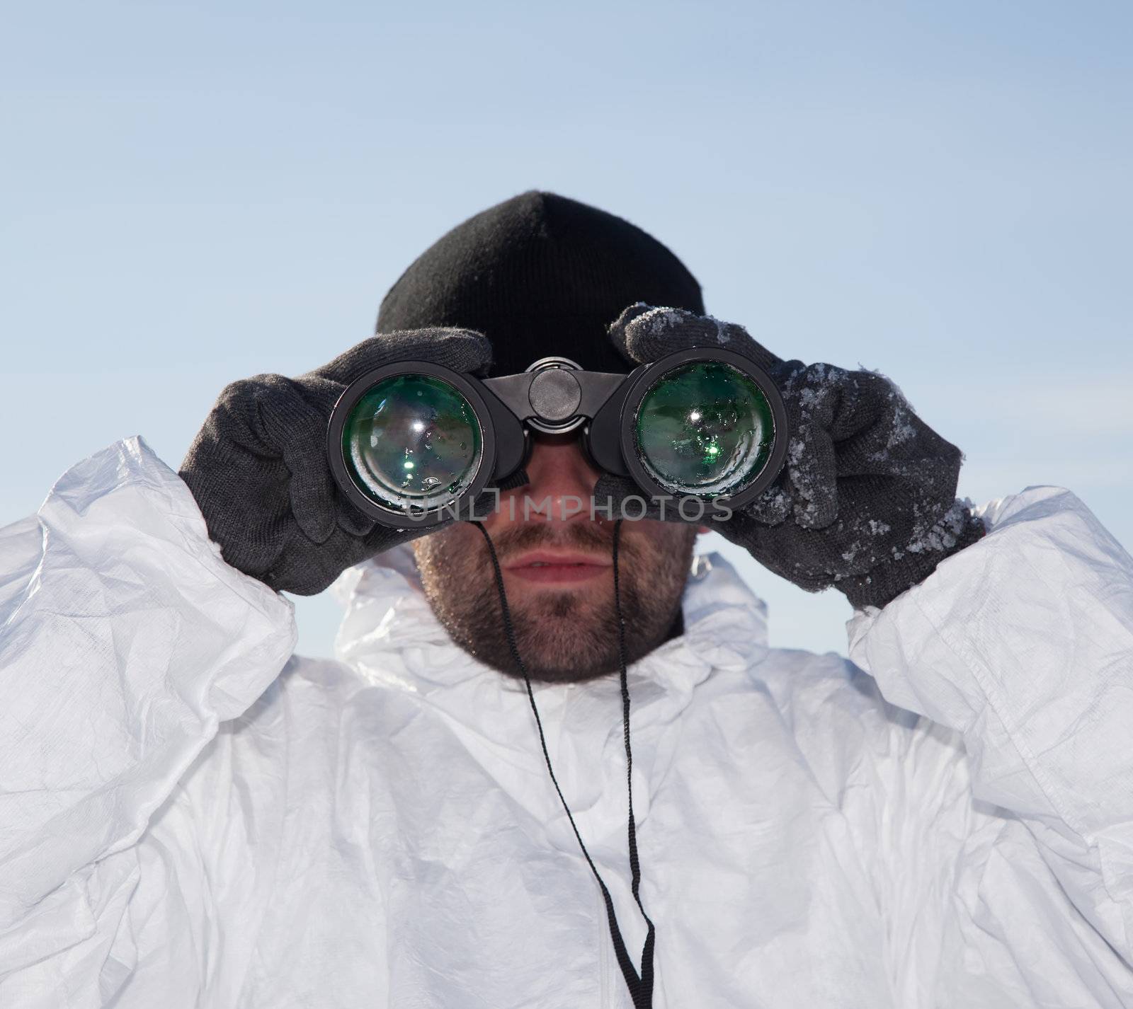 Special Forces soldier in white camouflage looking through binoculars against blue sky