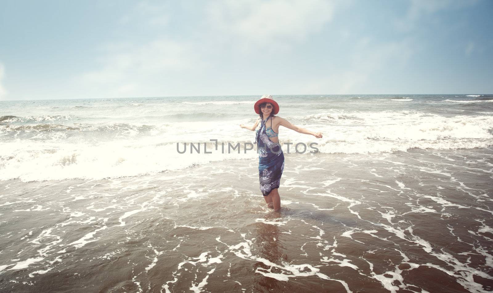 Happy brunette lady with hat and sunglasses standing at the beach