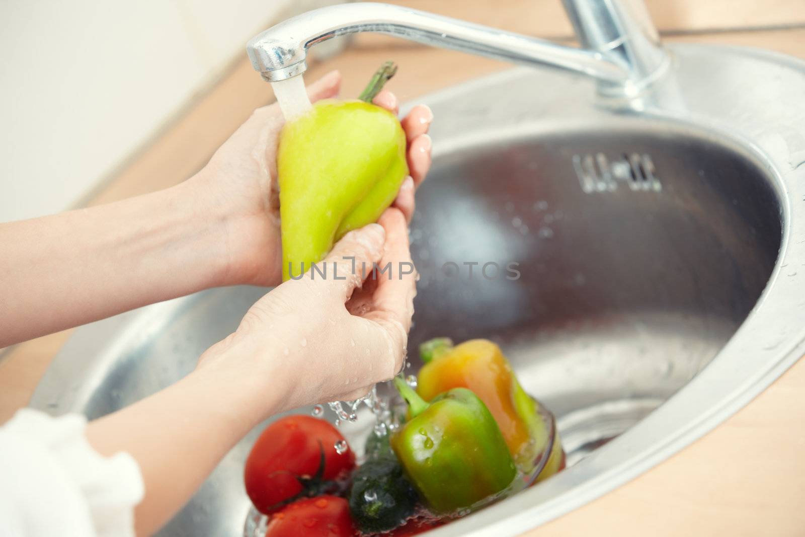 Hands of woman washing vegetables at her kitchen