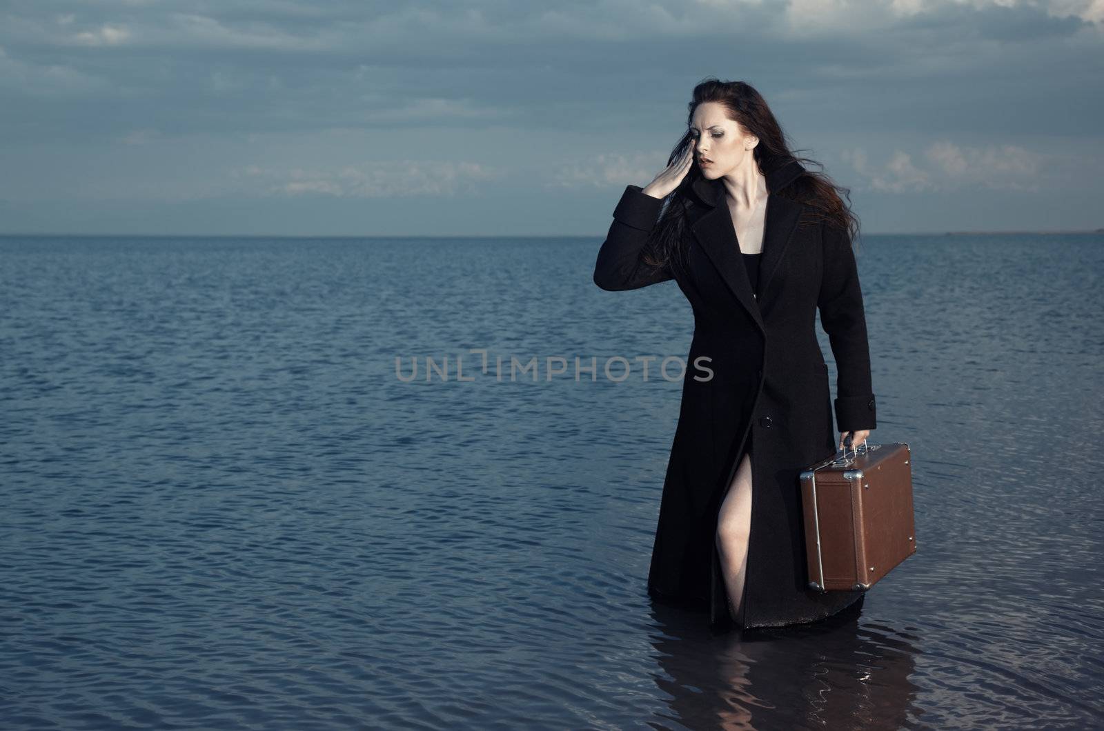 Woman in black coat standing in the sea with luggage