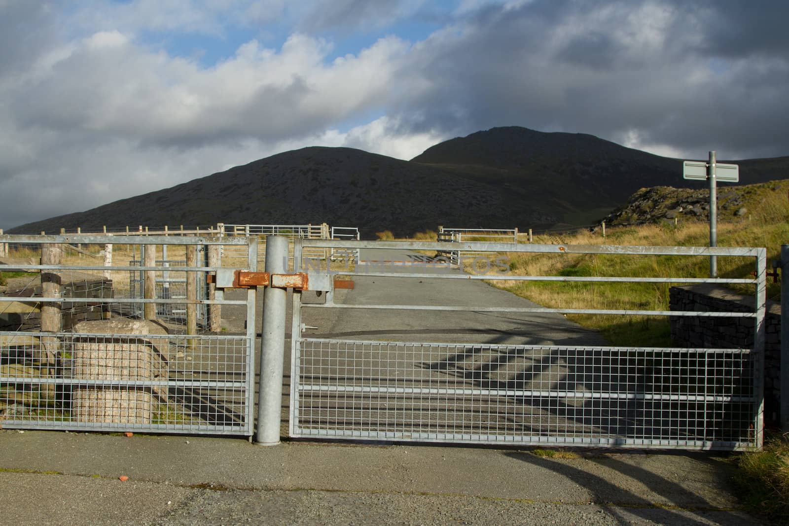 A road with locked metal security gates with mountains in the background.