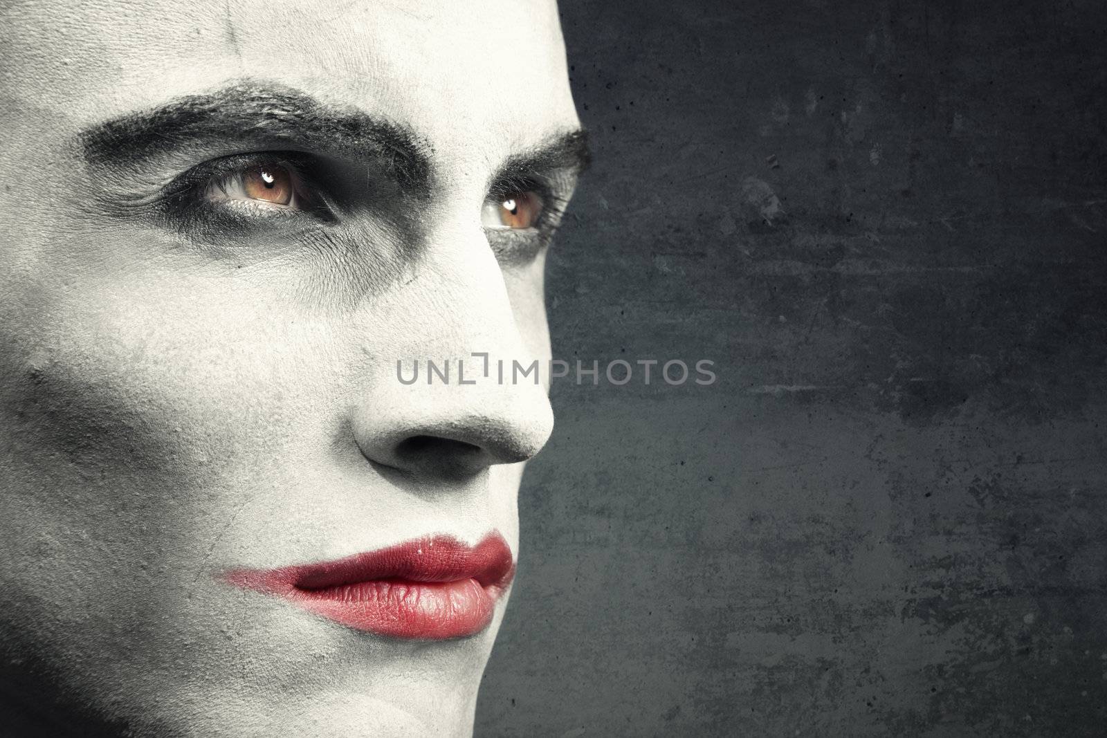 Man with vampire makeup on a dark grungy background. Natural makeup and background. Text can be added onto the empty space