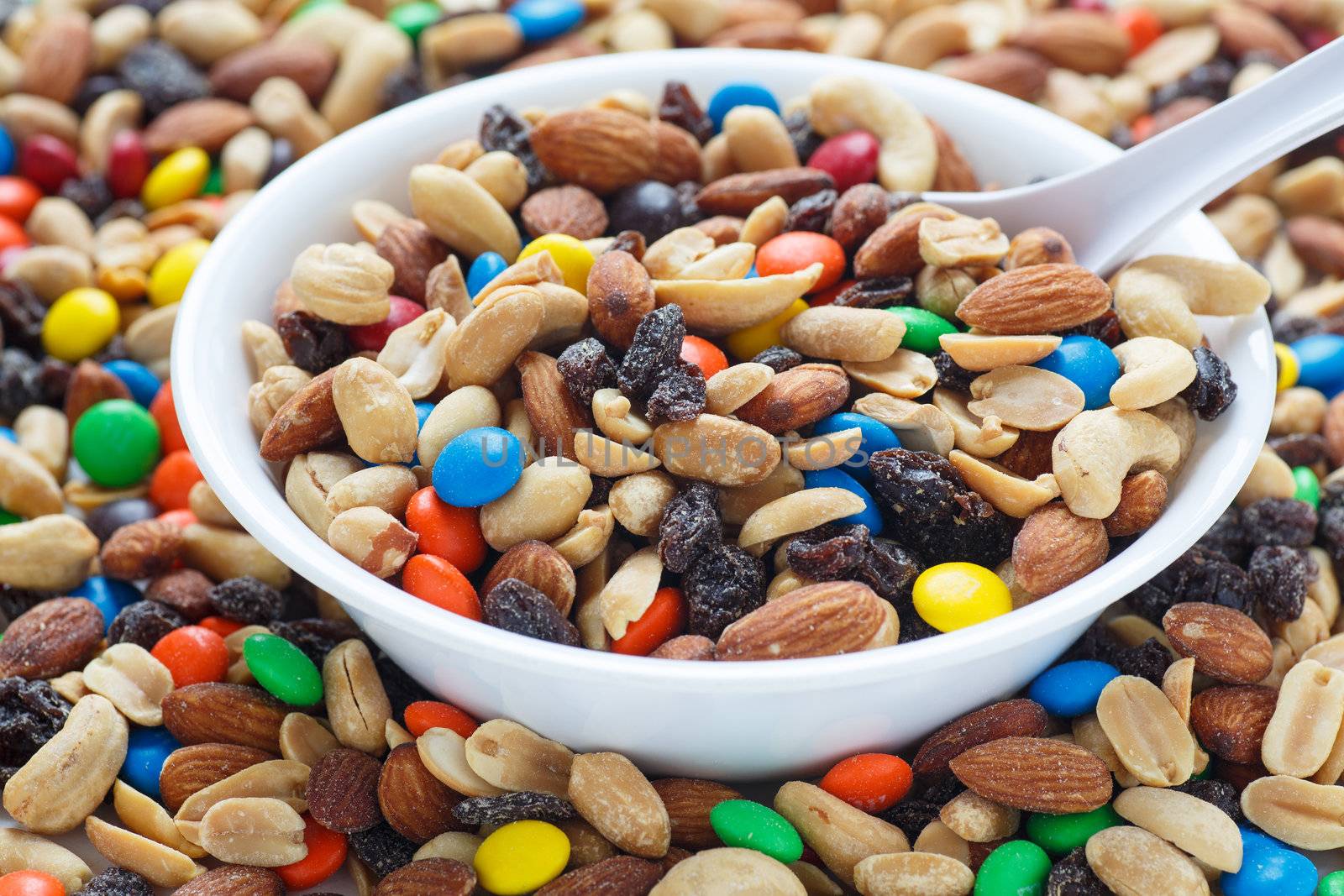 Colorful trail mix in a white bowl with spoon