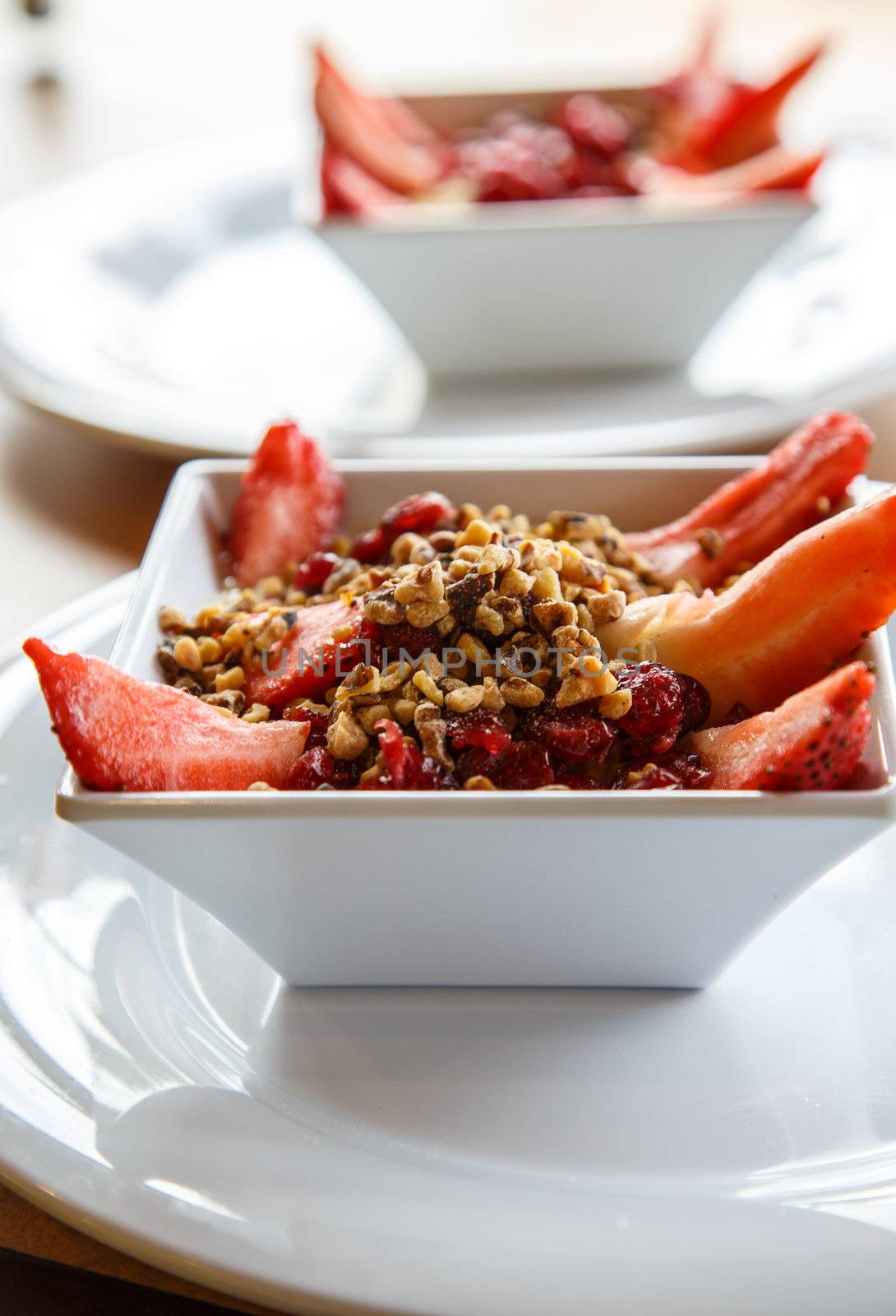 Steel-cut oatmeal in white bowl on white plate with strawberries, dried cranberries and walnuts