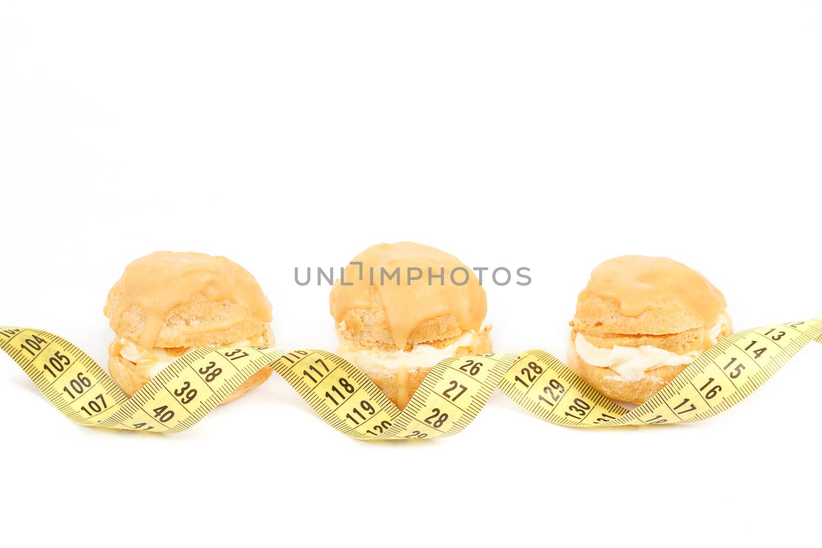 concept of slimming, caramel cakes with measuring tape on white background