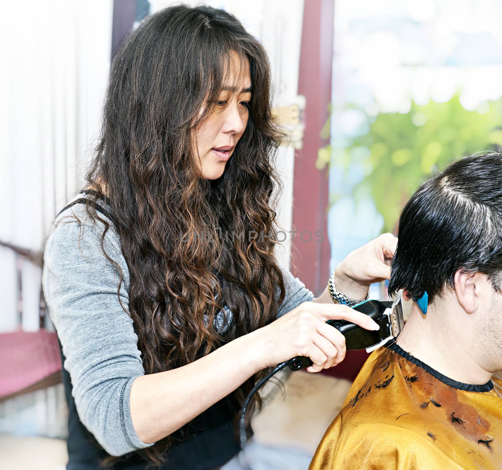 Hairdresser cutting hair in her salon with trimmer