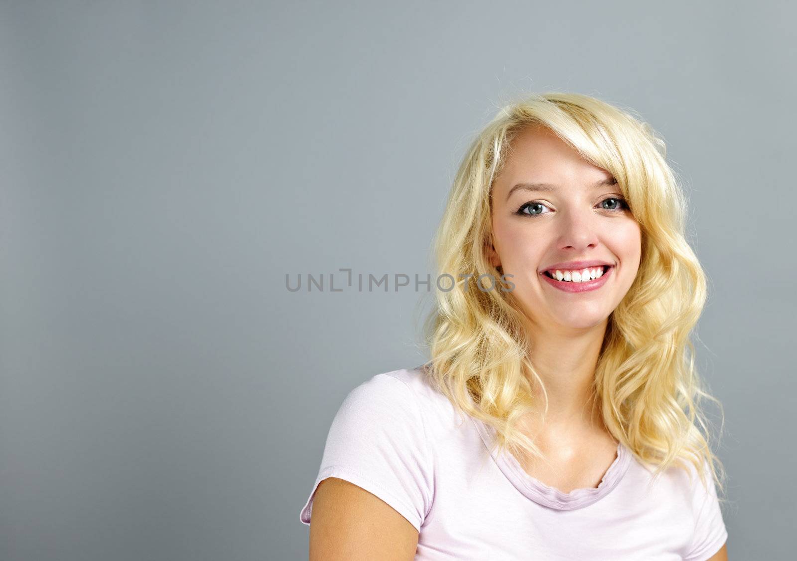 Portrait of smiling young blonde caucasian woman on grey background