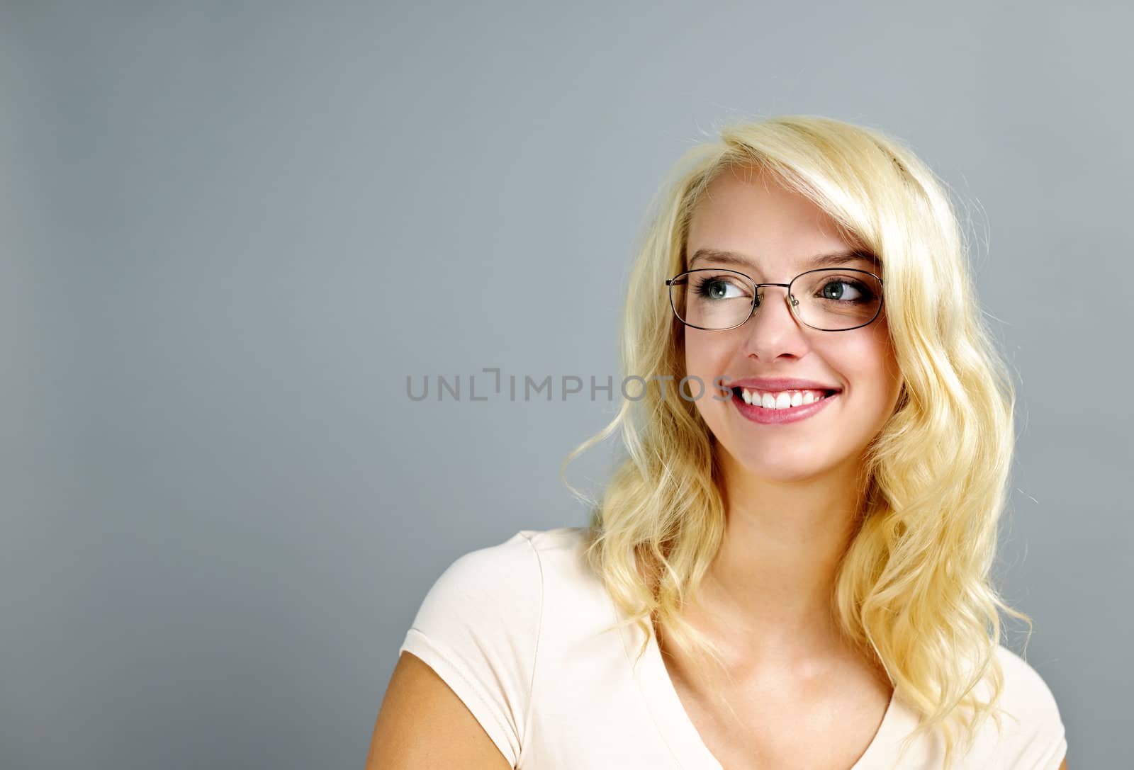 Smiling young woman wearing glasses looking to the side on grey background