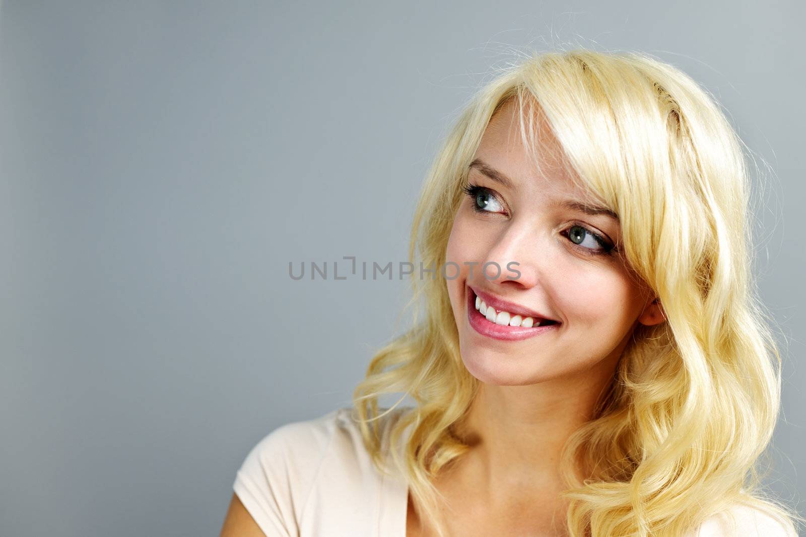 Portrait of smiling young blonde woman looking to the side on grey background
