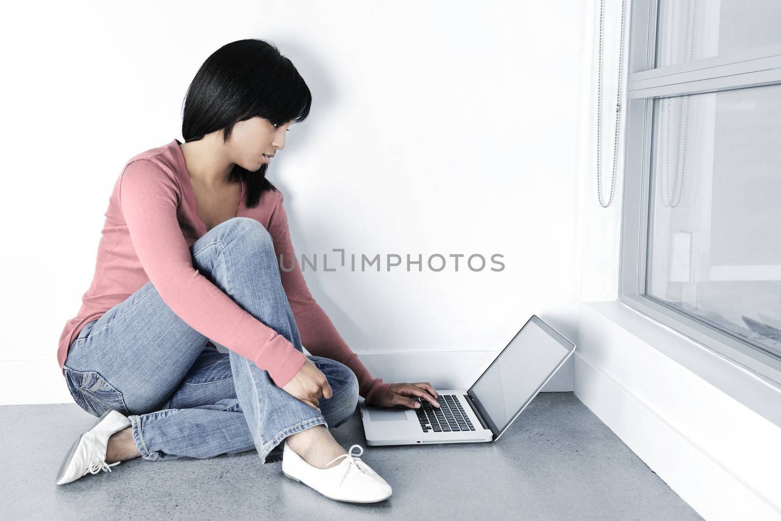 Young black woman with computer sitting on floor looking at laptop