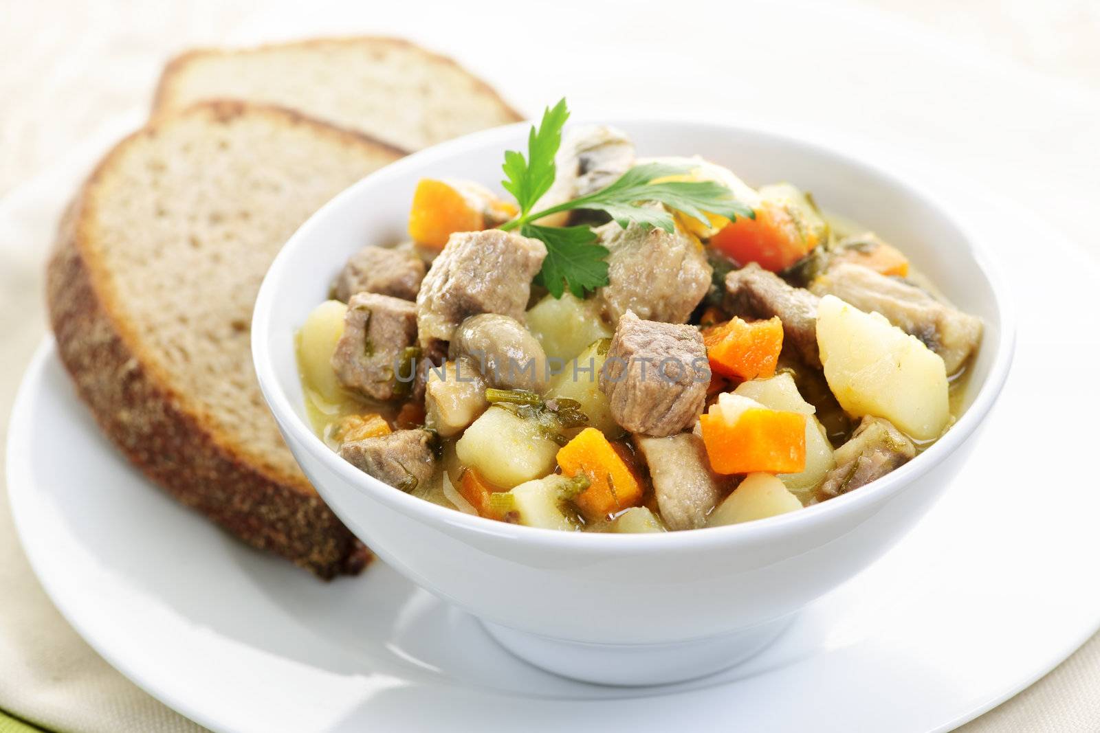 Bowl of hearty beef stew with vegetables served with rye bread