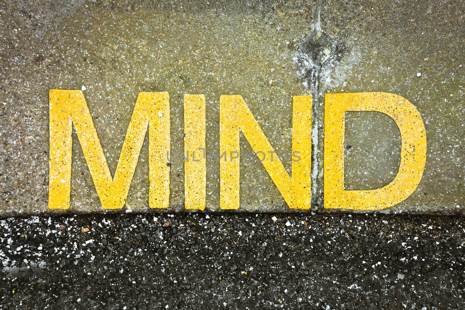 Mind written in yellow paint on a tarmac surface