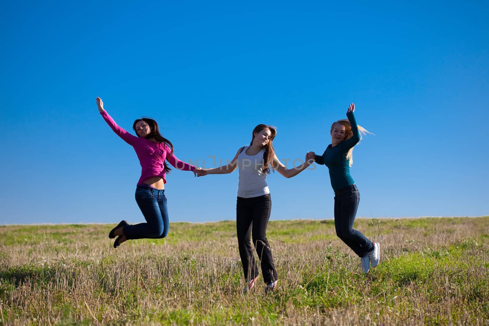 three young beautiful woman jumping into the field against the sky