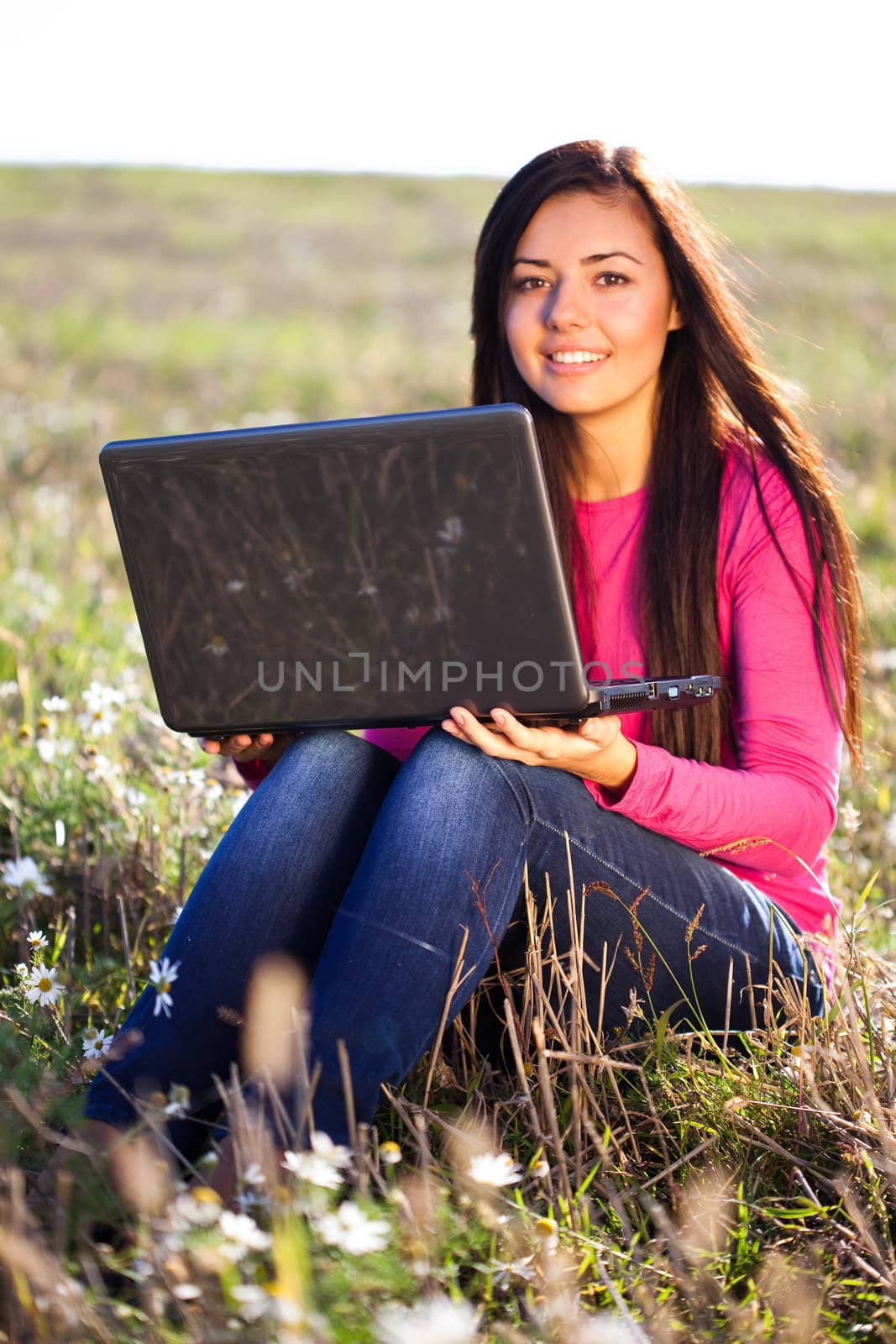 young beautiful woman with a laptop sitting in the field on sky background 