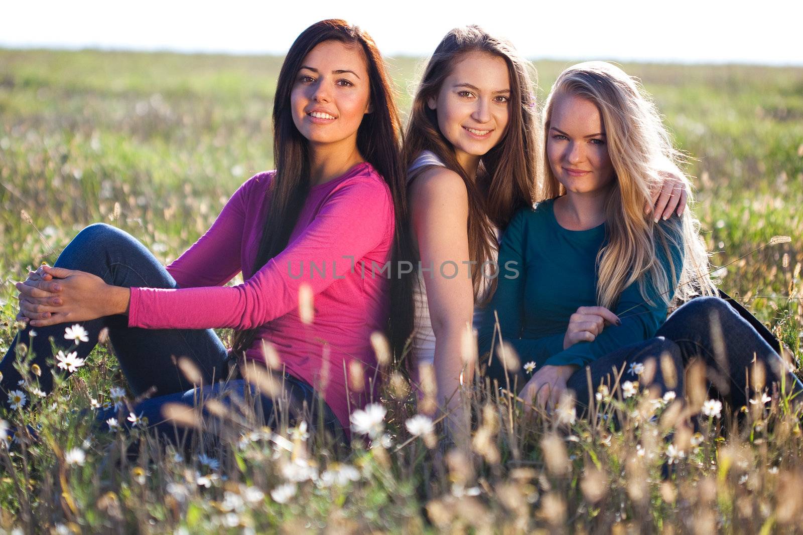 three young beautiful woman sitting in a field on the  sky backg by jannyjus