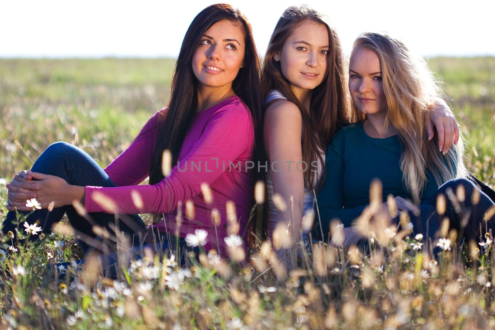 three young beautiful woman sitting in a field on the  sky background 