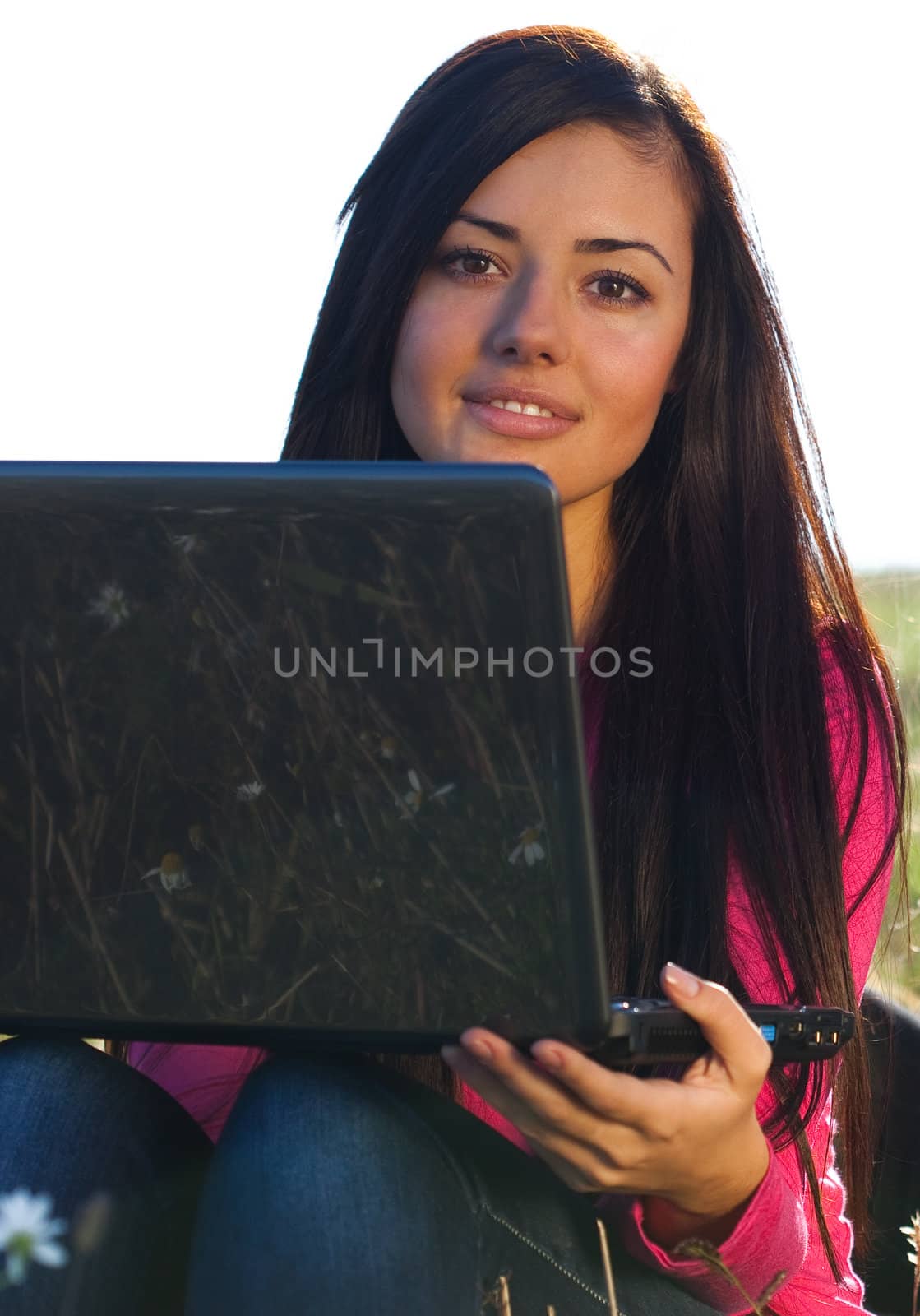 young beautiful woman with a laptop sitting in the field on sky background 