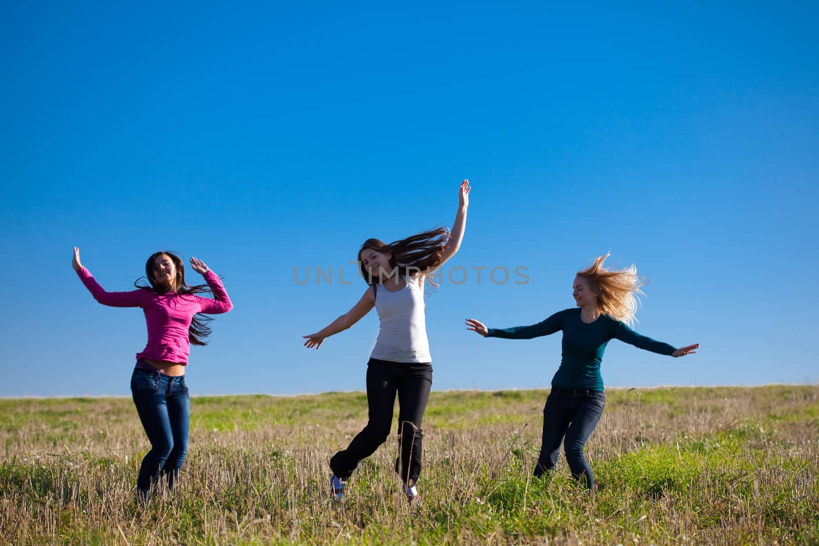 three young beautiful woman jumping into the field against the sky
