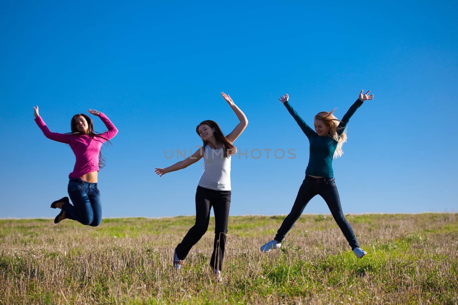 three young beautiful woman jumping into the field against the s by jannyjus