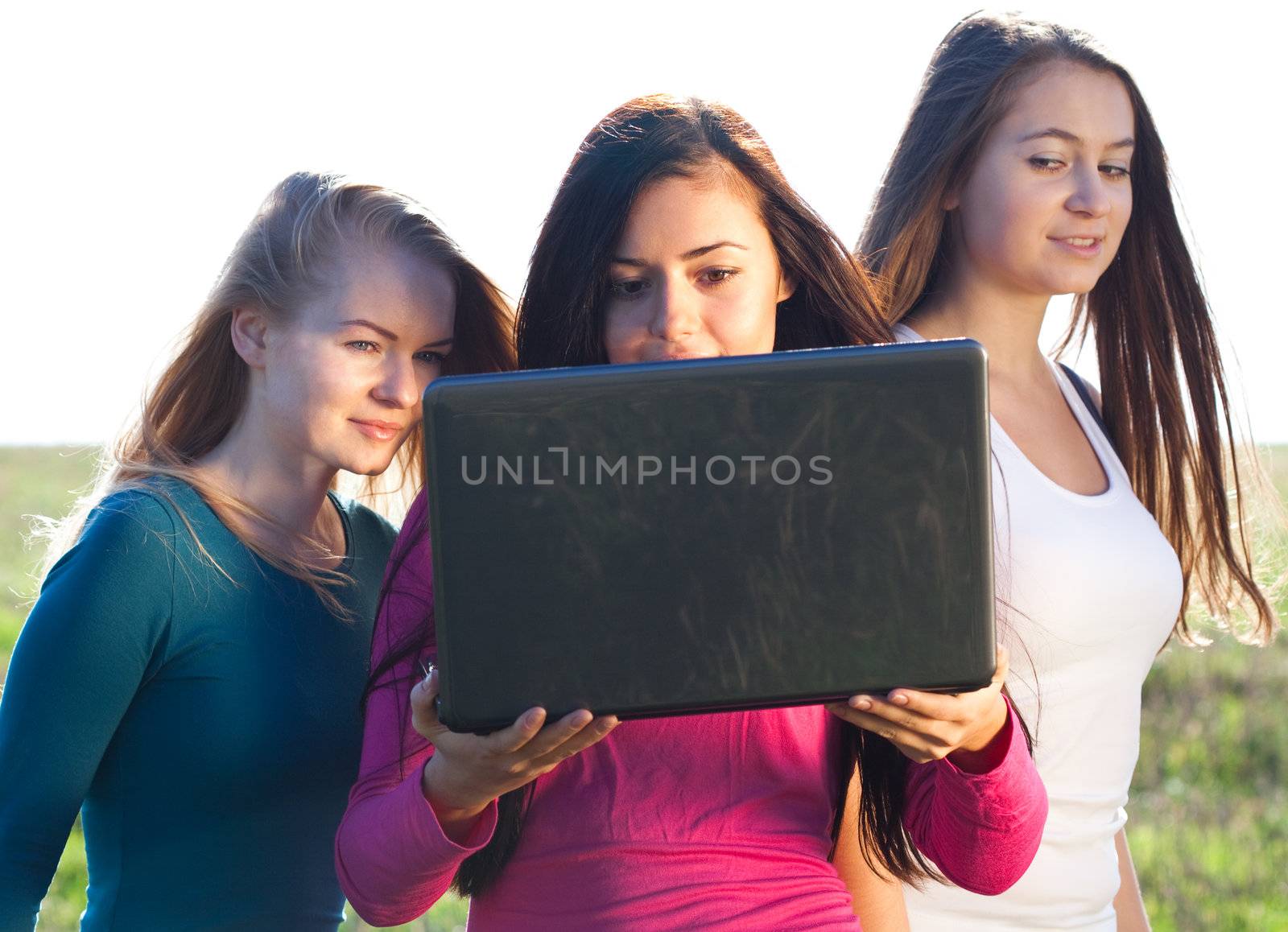 three young beautiful woman with a laptop in the field on sky ba by jannyjus