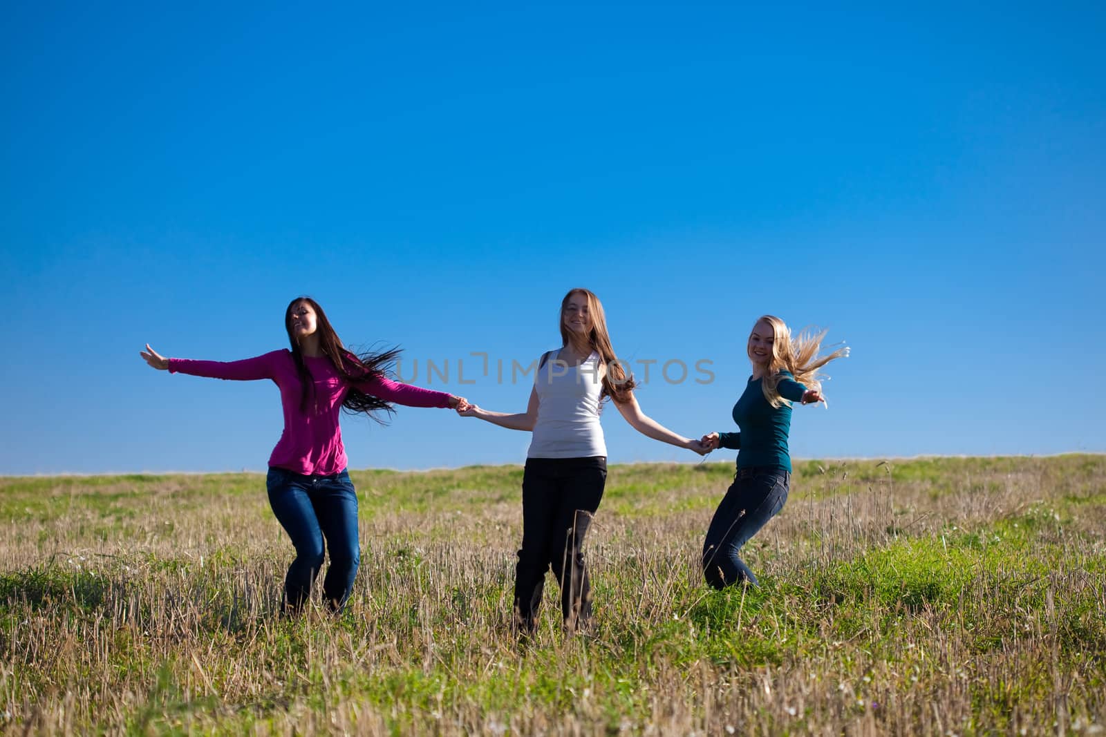 three young beautiful woman jumping into the field against the s by jannyjus