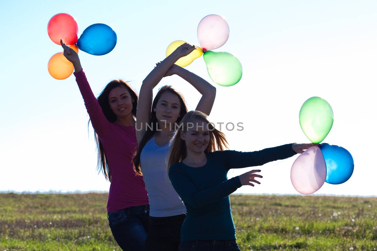 three young beautiful woman with balloons into the field against the sky