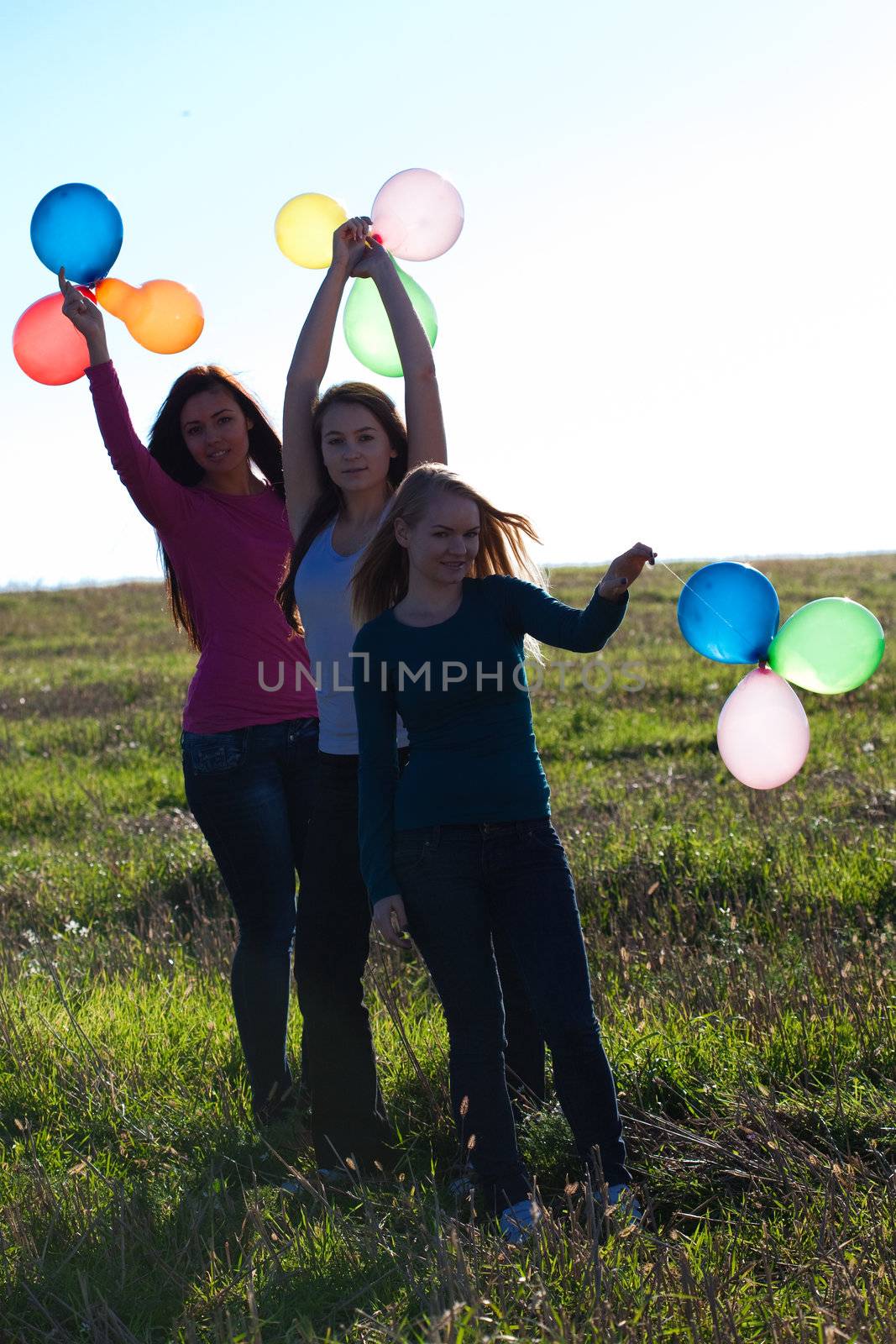 three young beautiful woman with balloons into the field against the sky