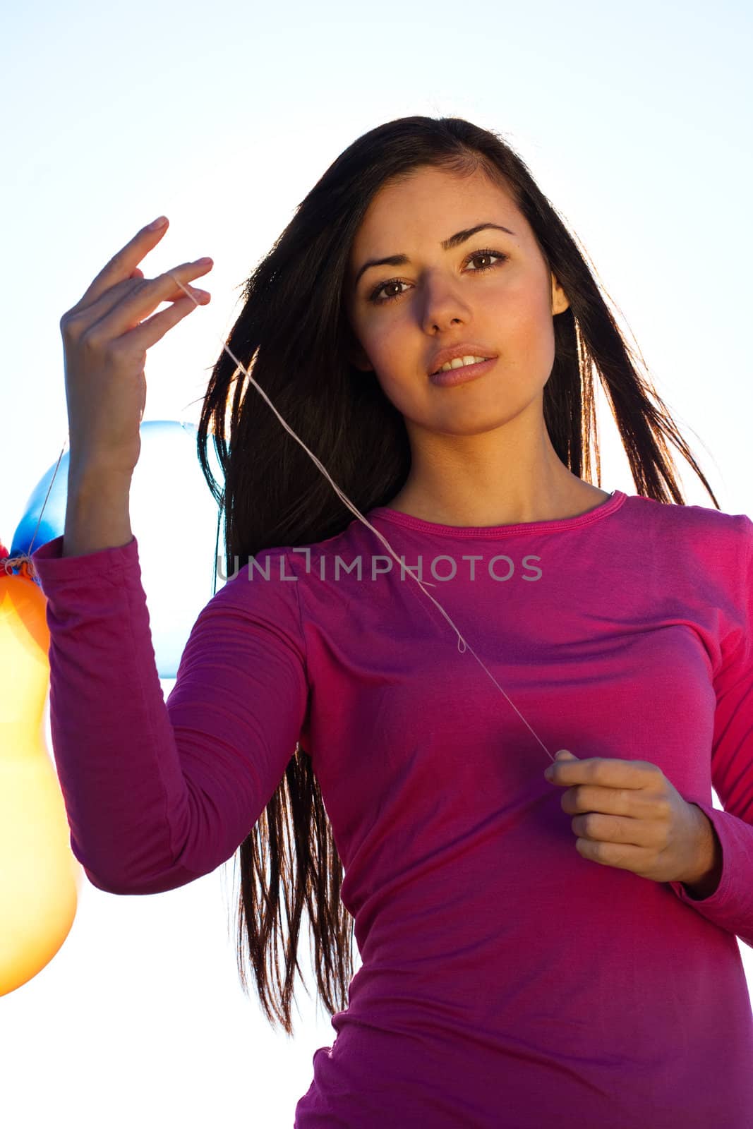 young beautiful woman with balloons into the field against the sky