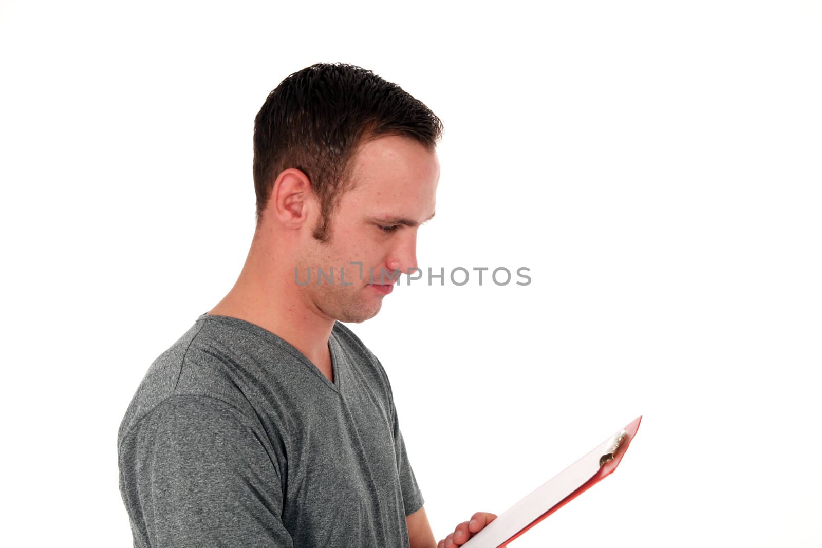 Upper body portrait of a young man in a casual t-shirt standing sideways reading notes on a clipboard isolated on white