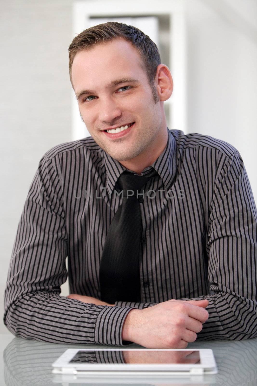 Successful happy man sitting at his desk with a tablet in front of him smiling at the camera
