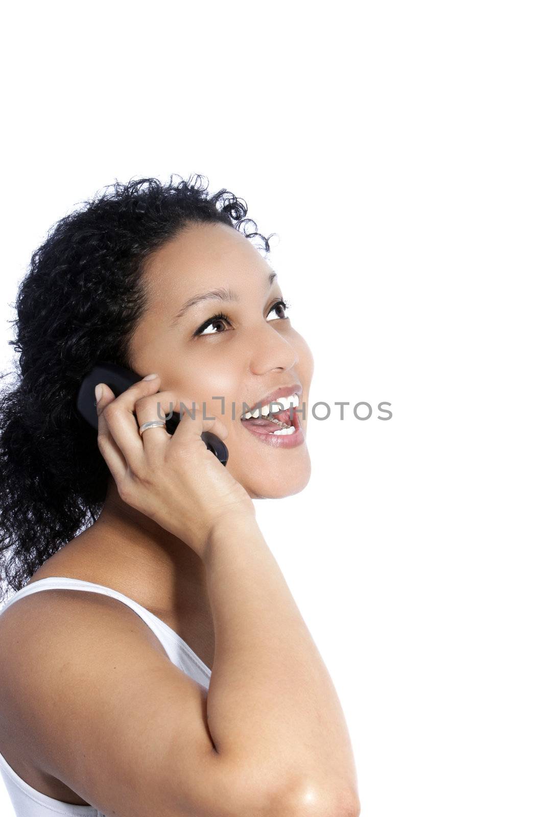 Beautiful young African American woman laughing as she listens to a conversation on her mobile phone, standing sideways isolated on white with copyspace