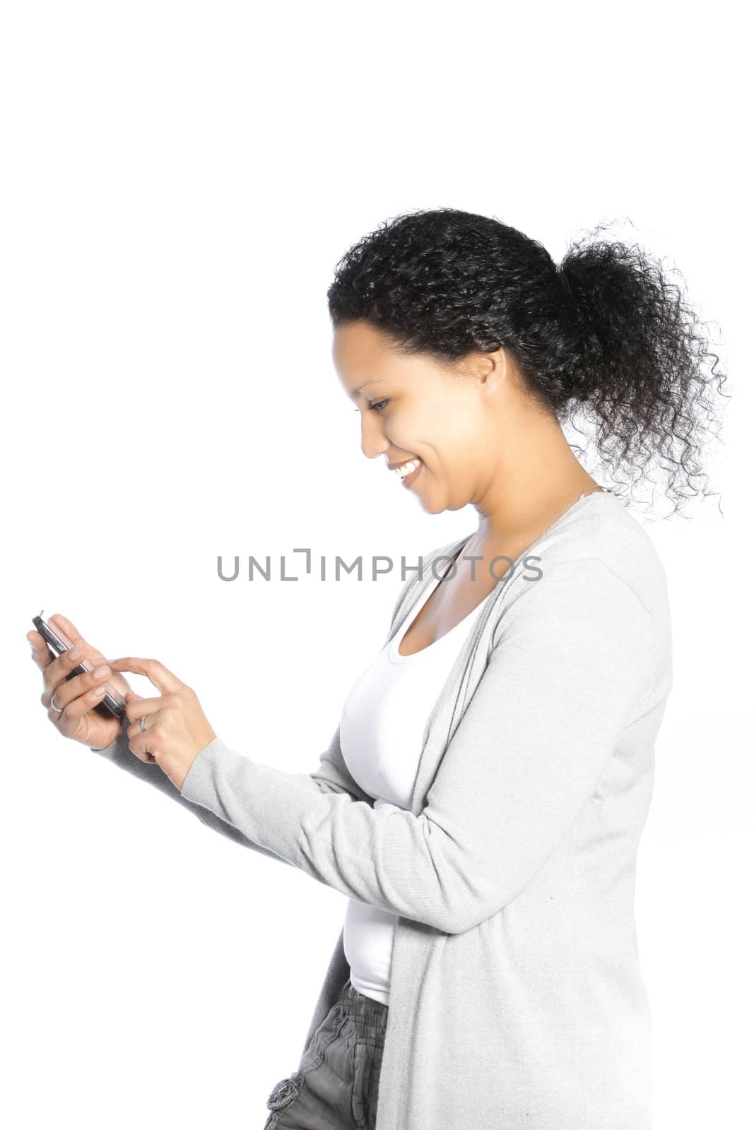 Smiling African American woman standing sideways sending an SMS or text message on her mobile phone isolated on white