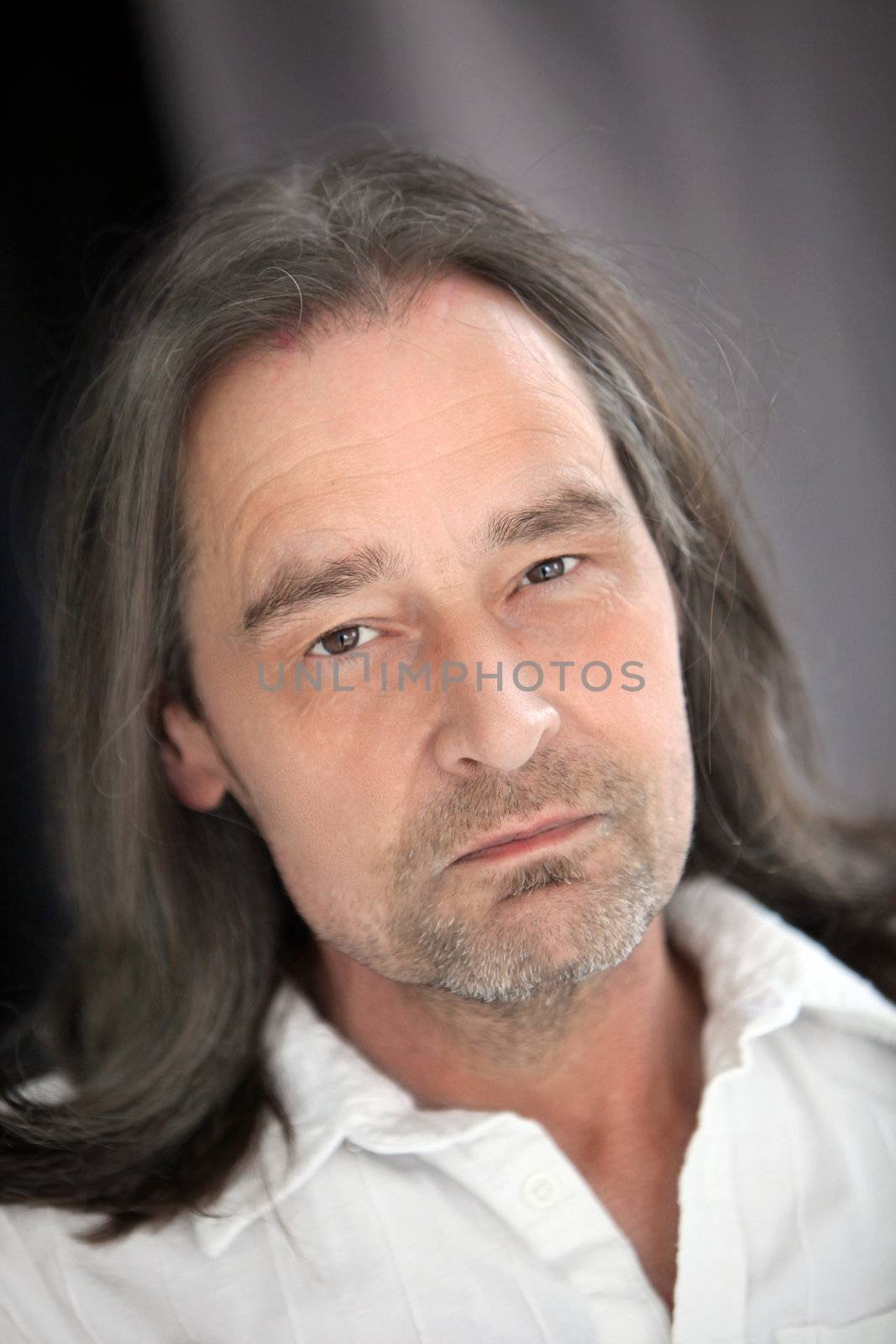 Closeup portrait of a serious handsome middle-aged unshaven man with long shoulder length hair