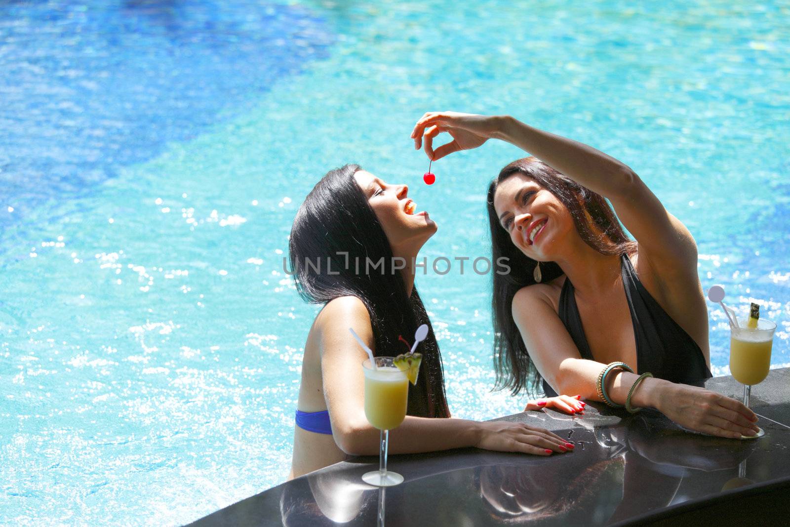 Two beautiful women relaxing in swimming pool with cocktails