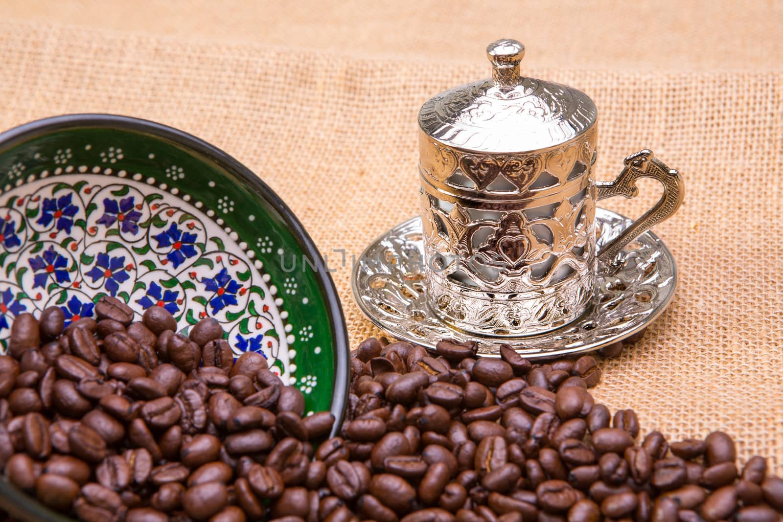 Authentic Turkish coffee cup with coffee beans. Coffee beans spilled on burlap from hand painted pottery.