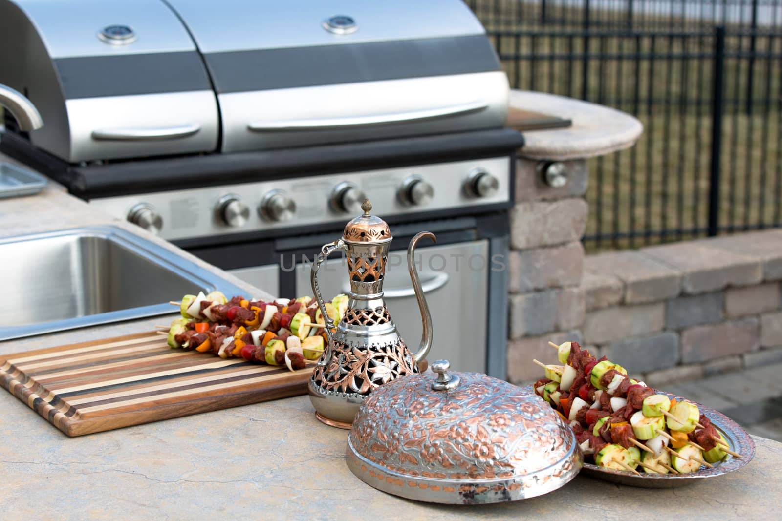 Skewers are in the traditional and authentic looking copper plate with complimenting pitcher. Meat skewers with vegetables at the outdoor kitchen on the concrete counter top.