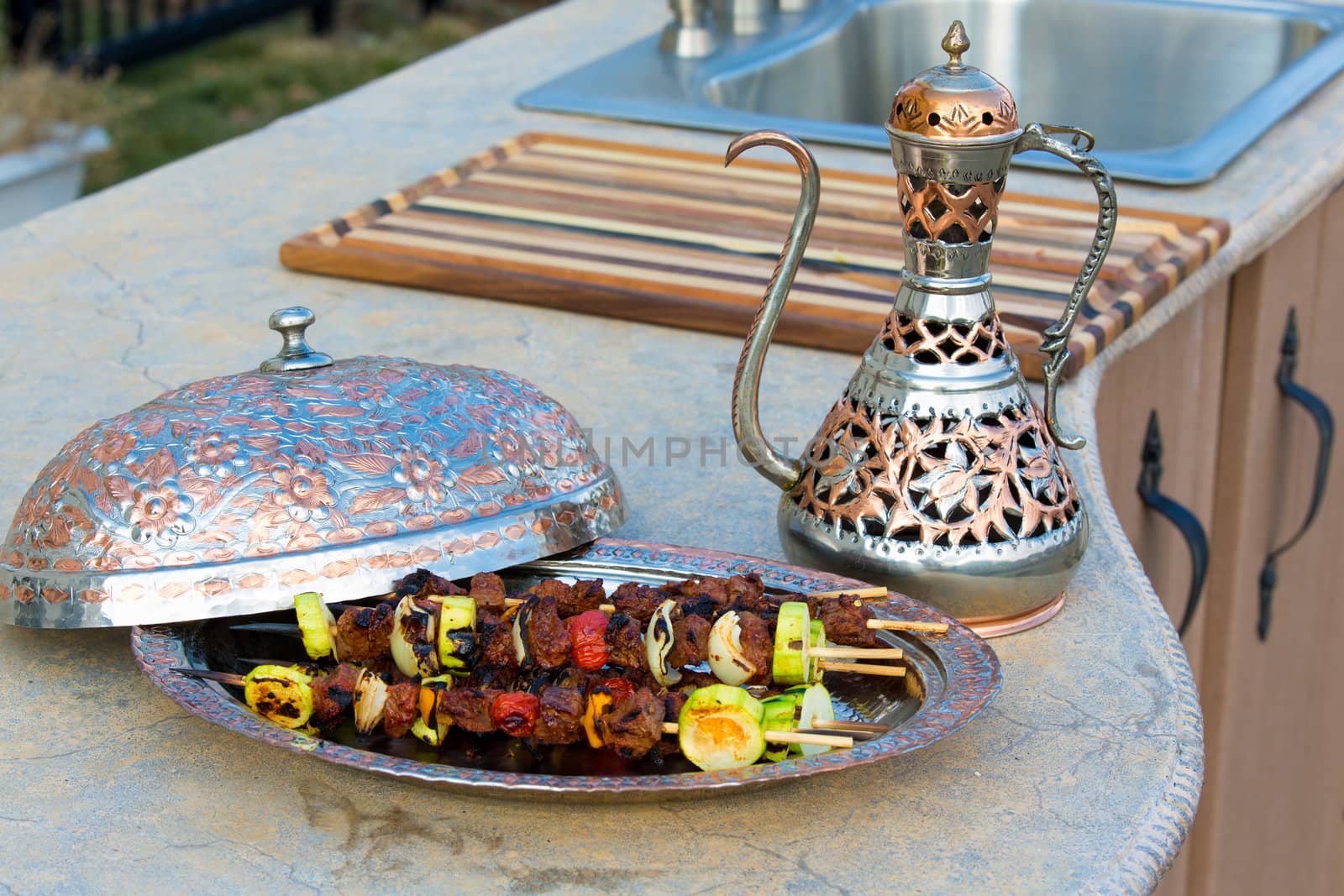 Sish skewers with vegetables presented in a copper bowl on a concrete counter top kitchen along with a matching copper pitcher.