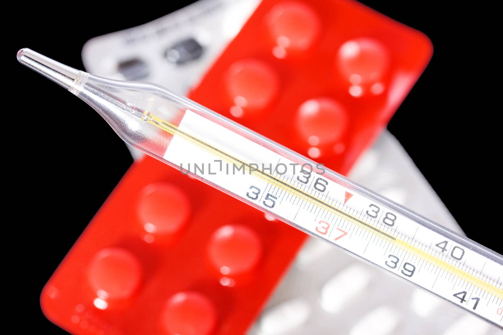 Thermometer and pills on black background