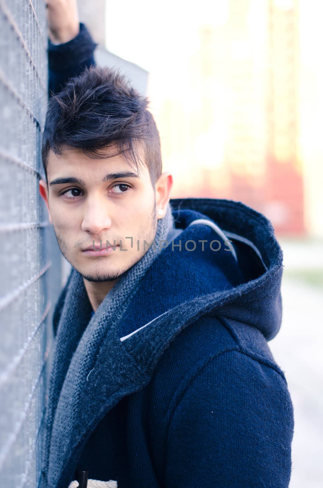 Good looking young man leaning against metal grid, urban setting and environment